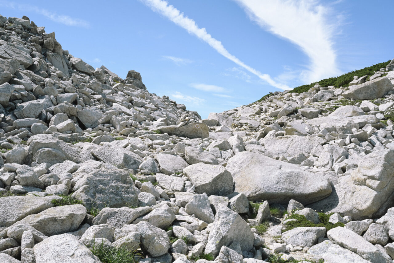 白い岩が積み重なった登山道を登る